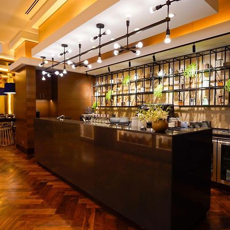 Jabal Omar Hyatt Regency Makkah Hotel Mecca Exterior foto The photo shows a modern bar area in a restaurant. The bar features a sleek, dark countertop and is backed by a decorative arrangement of shelves that holds various bottles and plants. The lighting is warm and stylish, with multiple hanging pendant l