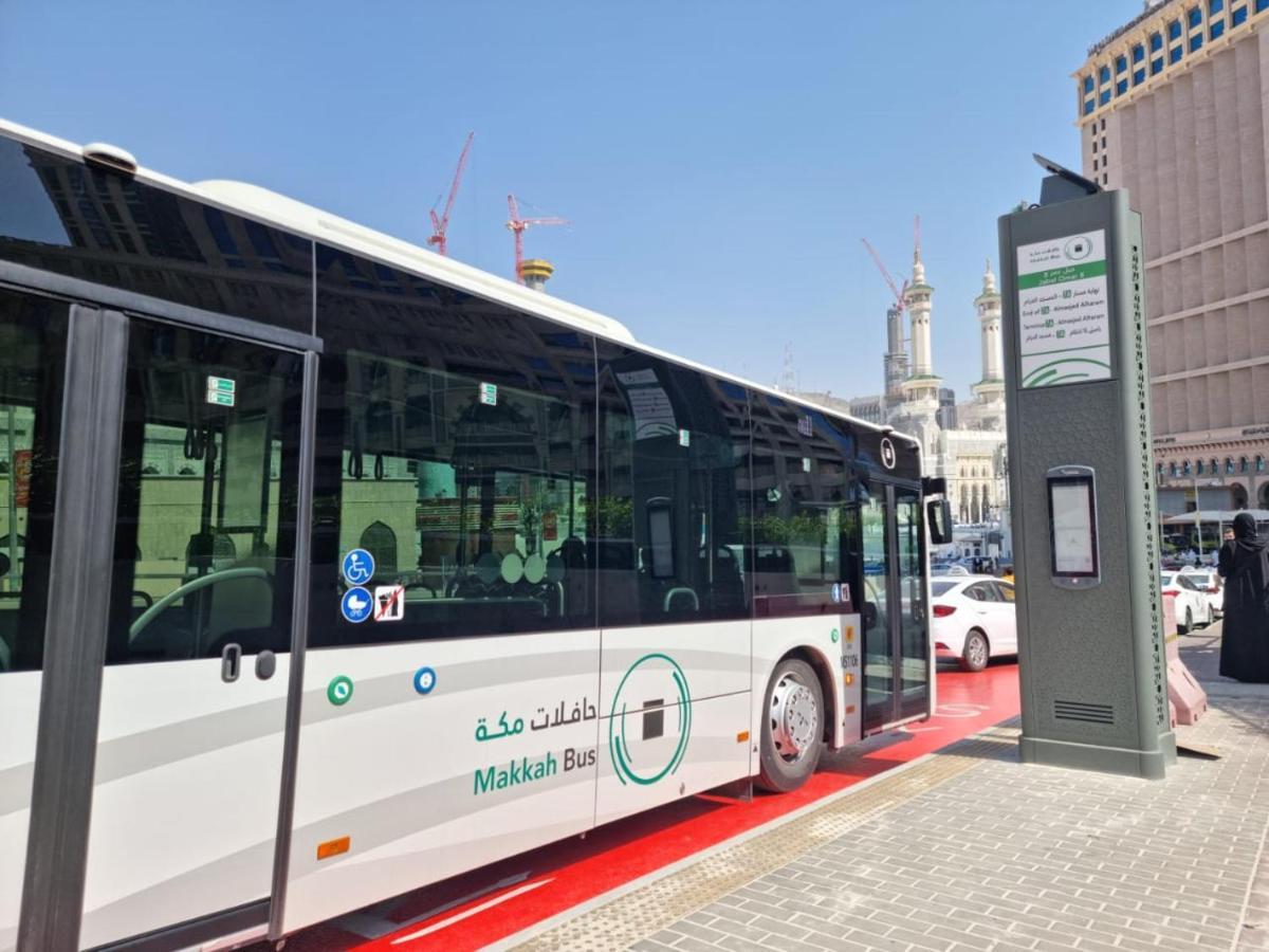 Jabal Omar Hyatt Regency Makkah Hotel Mecca Exterior foto The photo shows a public bus labeled "Makkah Bus," parked at a designated bus stop. The bus has a modern design and is predominantly white, with green accents. In the background, there are tall buildings and construction cranes, indicating a busy urb