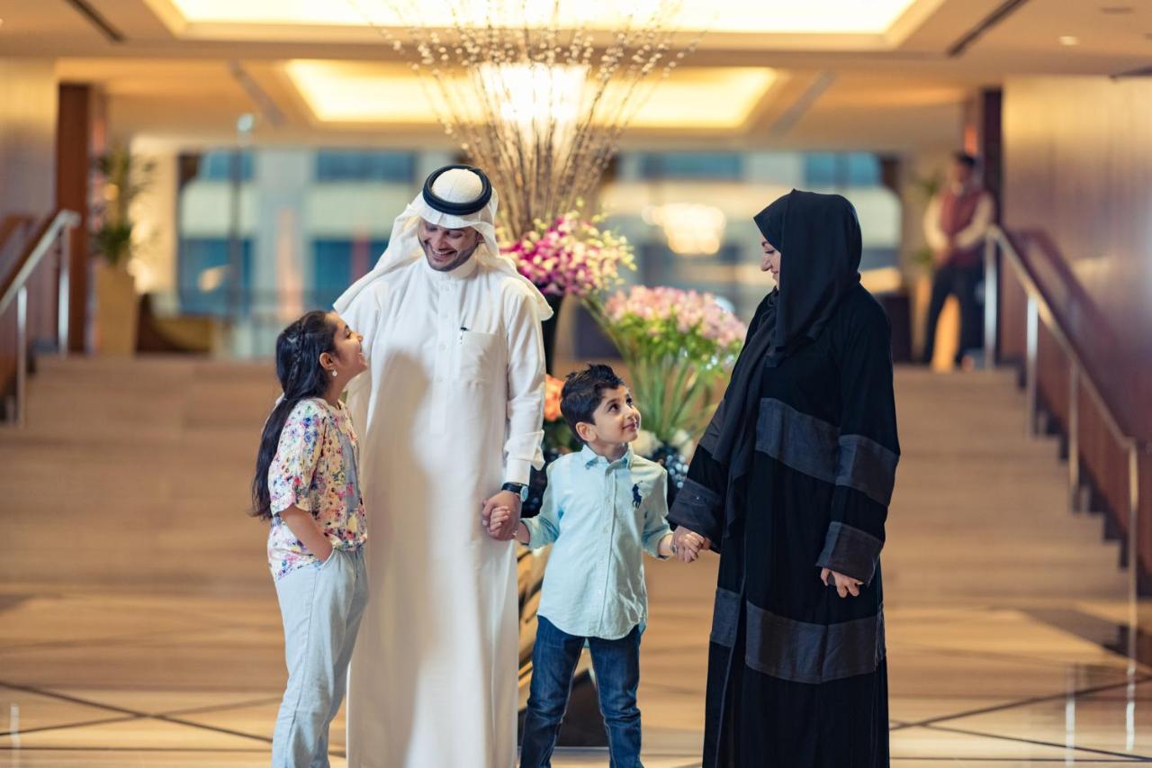 Jabal Omar Hyatt Regency Makkah Hotel Mecca Exterior foto The photo shows a family in a hotel lobby. There are two children, a boy and a girl, standing between their parents. The girl is smiling and looking up at her father, who is wearing traditional white attire and a headscarf. The boy is also smiling an