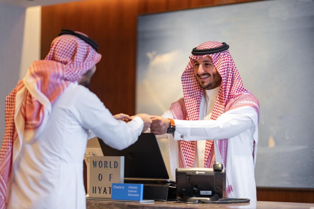 Jabal Omar Hyatt Regency Makkah Hotel Mecca Exterior foto The photo shows a scene at a hotel reception desk. A hotel staff member, dressed in traditional attire, is smiling and handing something to a guest, who is also wearing traditional clothing. The guest appears to be receiving a key or a document. The 