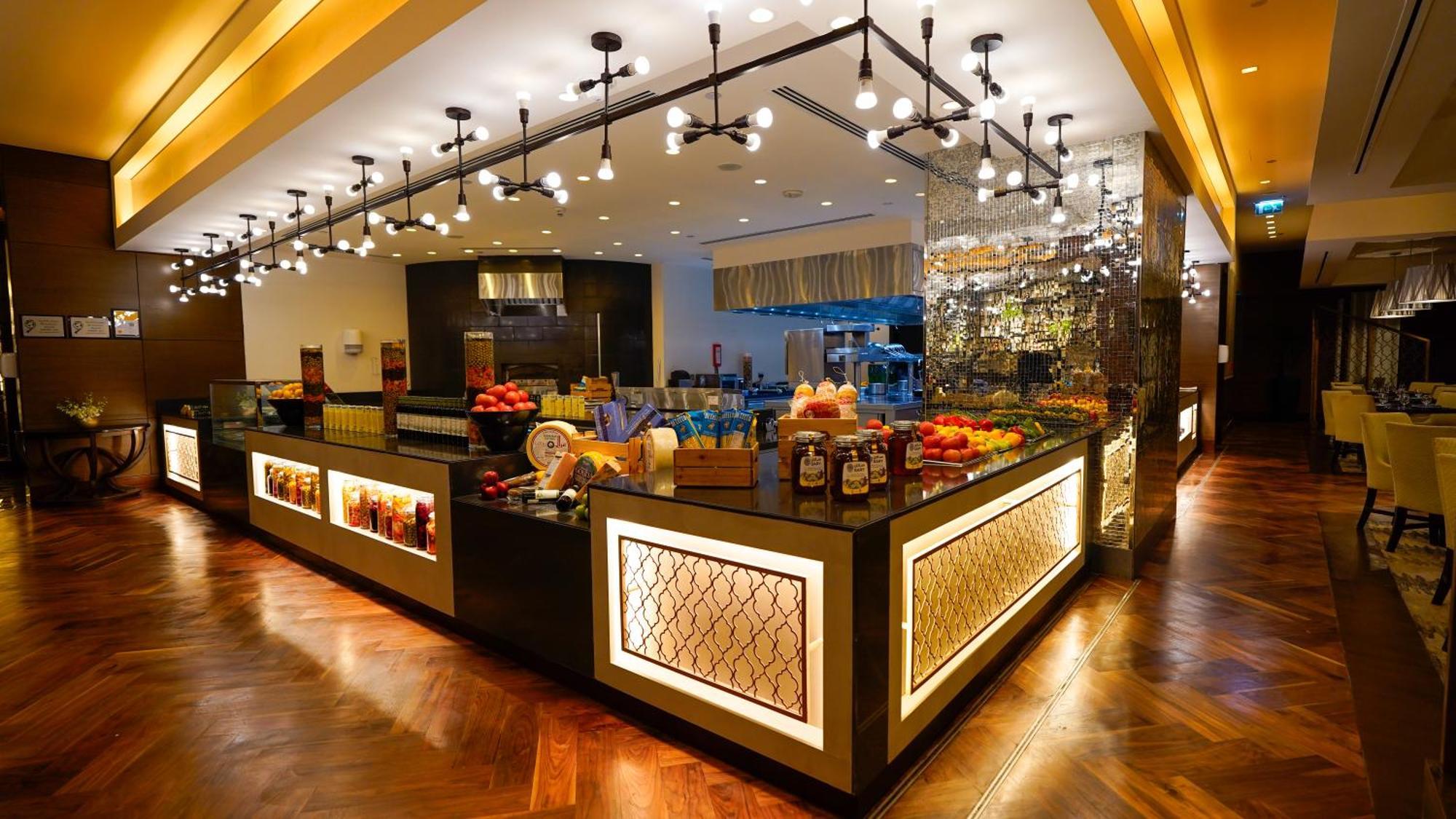 Jabal Omar Hyatt Regency Makkah Hotel Mecca Exterior foto The photo shows a stylish and modern buffet area in a restaurant or hotel. The design features a sleek counter with various food items displayed, including fresh fruits. The space is well-lit with pendant lights hanging from the ceiling, creating a w
