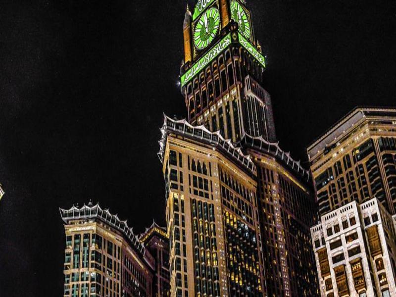 Jabal Omar Hyatt Regency Makkah Hotel Mecca Exterior foto The photo shows a tall building, which is a prominent feature of a city skyline, illuminated against a dark night sky. At the top of the building is a large clock tower, noticeable for its distinct green color, and intricate architectural details. Th