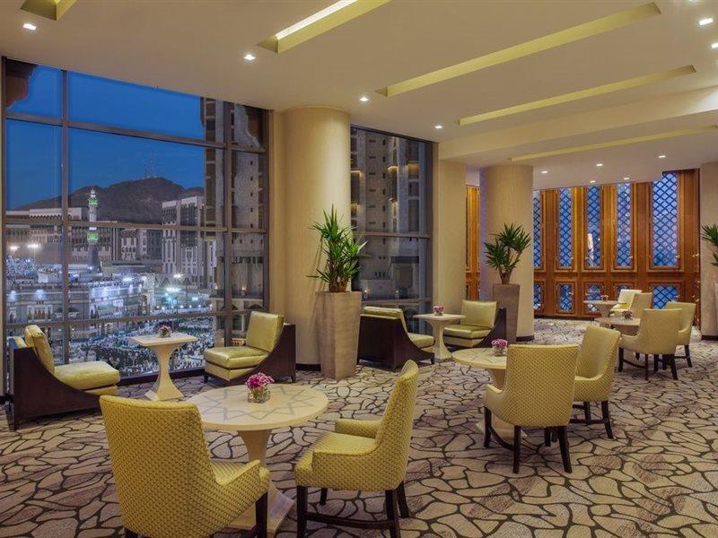 Jabal Omar Hyatt Regency Makkah Hotel Mecca Exterior foto The photo shows a modern, well-lit lounge or reception area. It features several small round tables surrounded by comfortable chairs, all in a soft yellow upholstery. The flooring is composed of stone tiles, adding a natural element to the decor. Lar