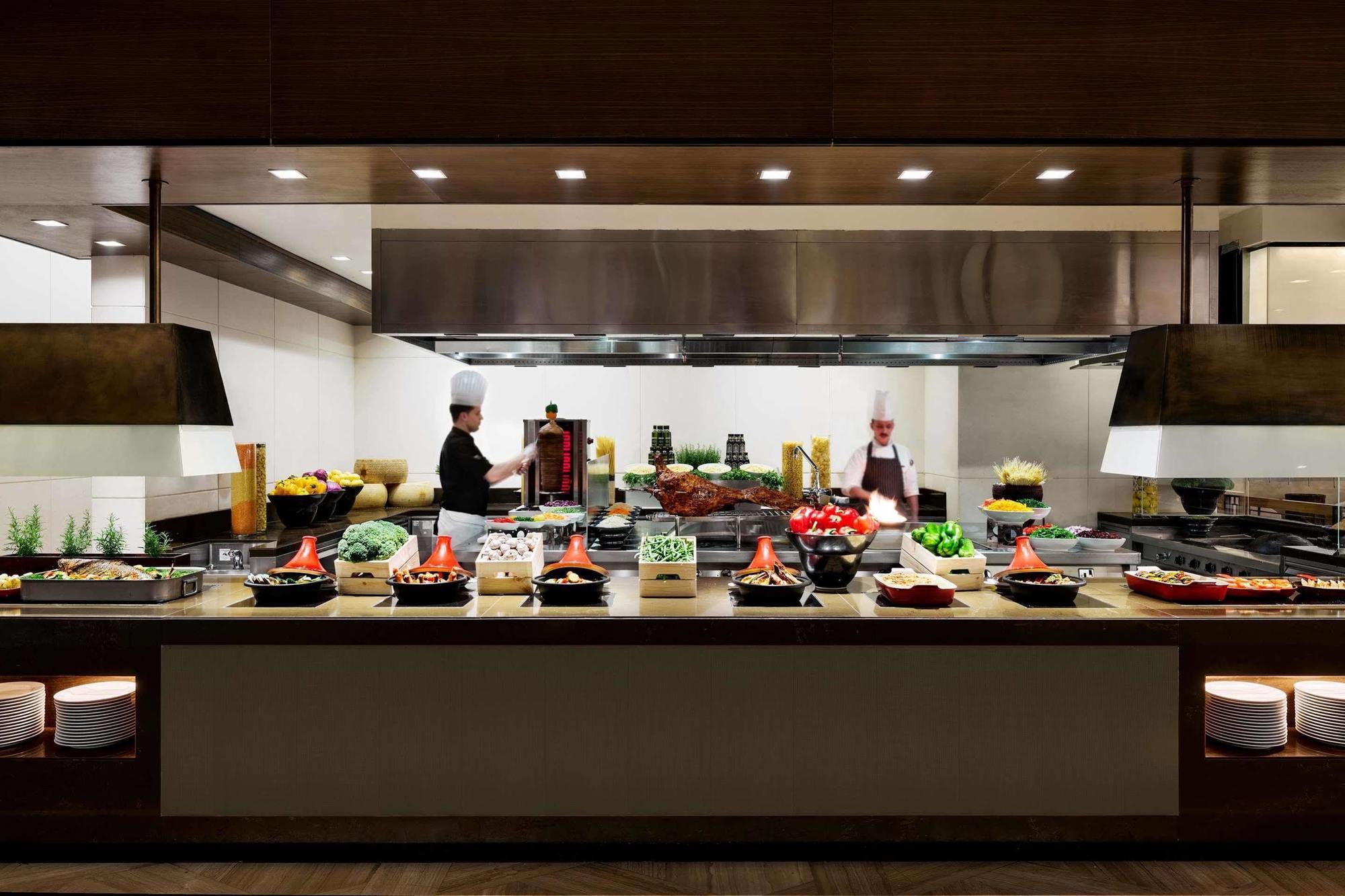 Jabal Omar Hyatt Regency Makkah Hotel Mecca Exterior foto The photo shows a well-organized kitchen or buffet area. In the foreground, there are several food stations displaying a variety of dishes, including fresh vegetables, meats, and other culinary items arranged in bowls or trays. Behind the counter, tw