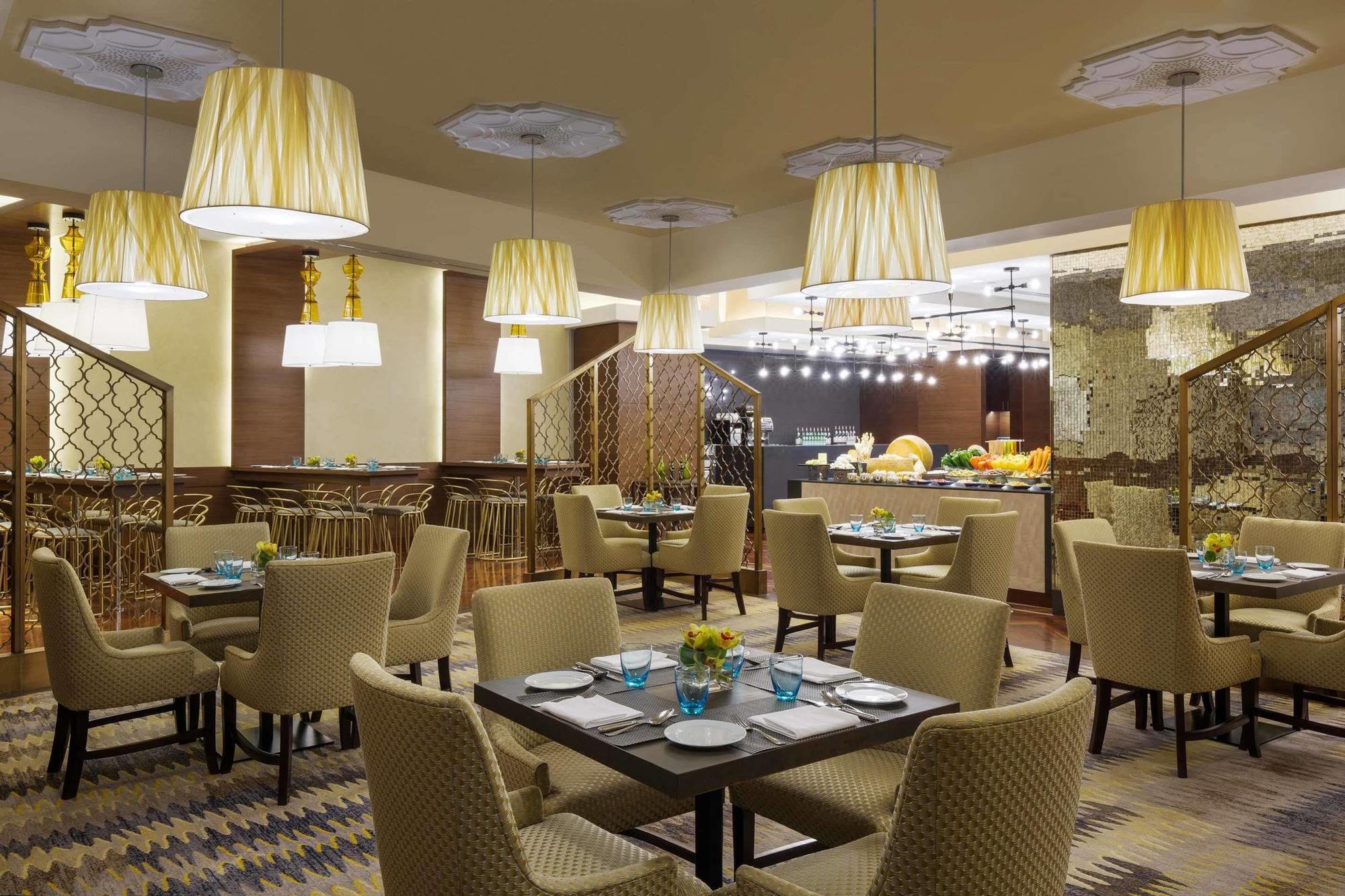 Jabal Omar Hyatt Regency Makkah Hotel Mecca Exterior foto The photo displays a modern restaurant interior. It features a series of round tables with beige upholstered chairs arranged neatly throughout the space. Each table is set with plates and blue-tinted glasses. The lighting is provided by stylish penda