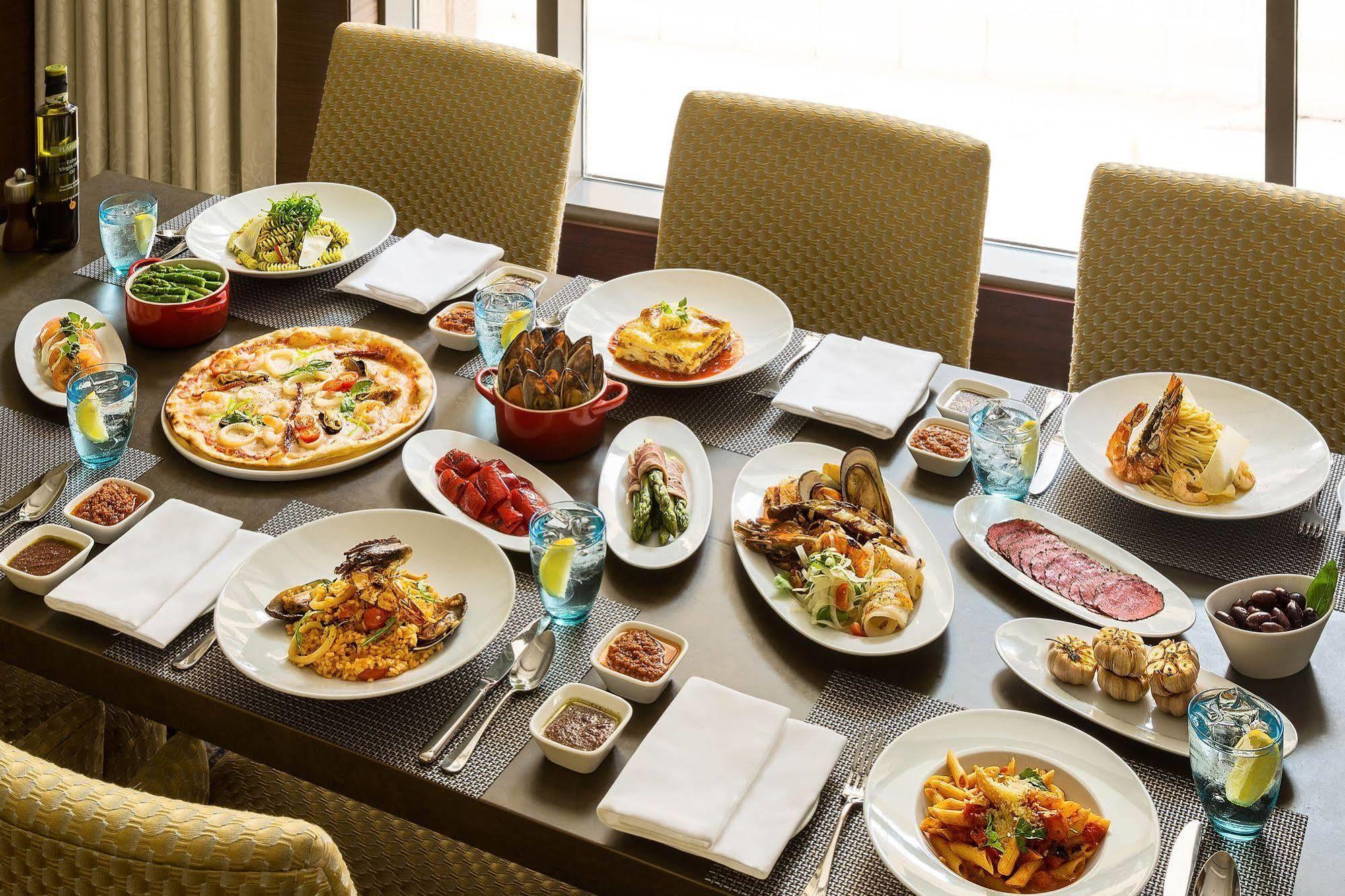 Jabal Omar Hyatt Regency Makkah Hotel Mecca Exterior foto The photo shows a large dining table set with various dishes, suggesting a festive or communal meal. There are several plates of food including:

- A pizza topped with vegetables and possibly meats.
- A serving of lasagna.
- A variety of pasta dishes