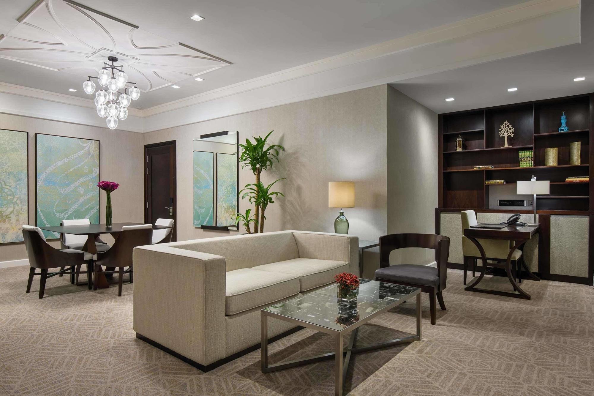 Jabal Omar Hyatt Regency Makkah Hotel Mecca Exterior foto The image shows a contemporary living space that includes a light-colored sofa and a glass coffee table. In the background, there is a dining area with a round table and chairs, along with framed artwork on the walls. A potted plant adds a touch of g