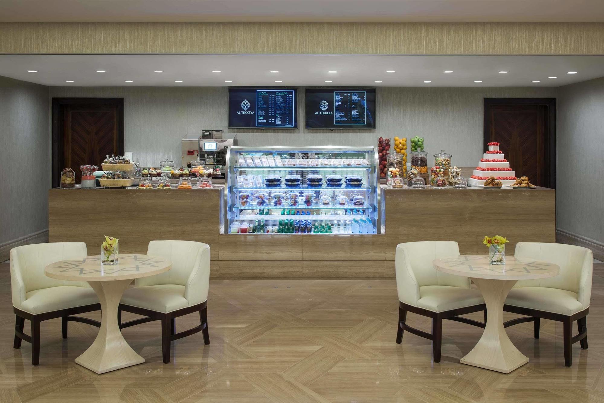 Jabal Omar Hyatt Regency Makkah Hotel Mecca Exterior foto The photo shows a quaint café or dessert shop interior. In the background, there's a neatly arranged counter displaying a variety of pastries and desserts, including cakes and sweets. Above the counter, two menus or screens display the offerings. In 