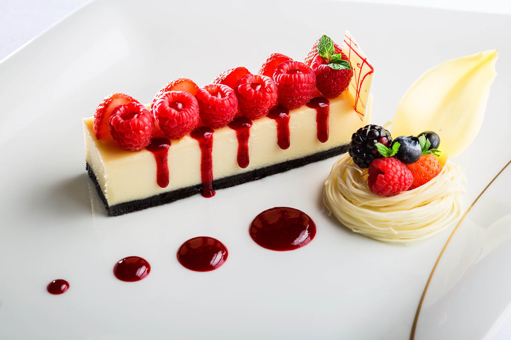 Jabal Omar Hyatt Regency Makkah Hotel Mecca Exterior foto The photo shows an elegantly plated dessert featuring a rectangular piece of cheesecake topped with fresh raspberries. The cheesecake is set on a dark crust, possibly made of chocolate or cookie crumbs. There are red fruit coulis drizzled artfully ar