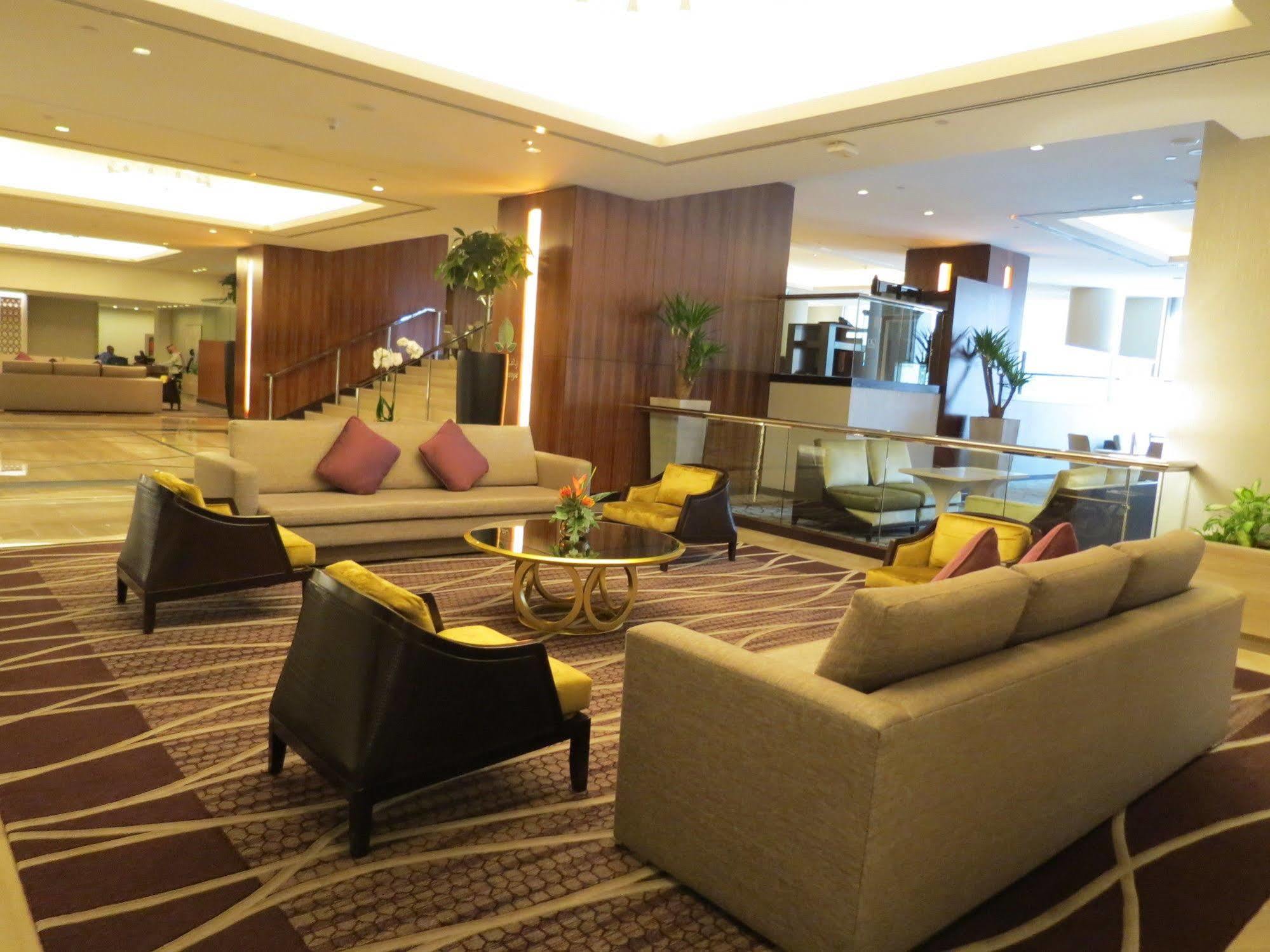 Jabal Omar Hyatt Regency Makkah Hotel Mecca Exterior foto The photo shows a modern and stylish lobby or lounge area. It features two large sofas with a light color and several cushions in shades of purple. There are also two armchairs with a darker finish and yellow cushions. In the center, there is a round