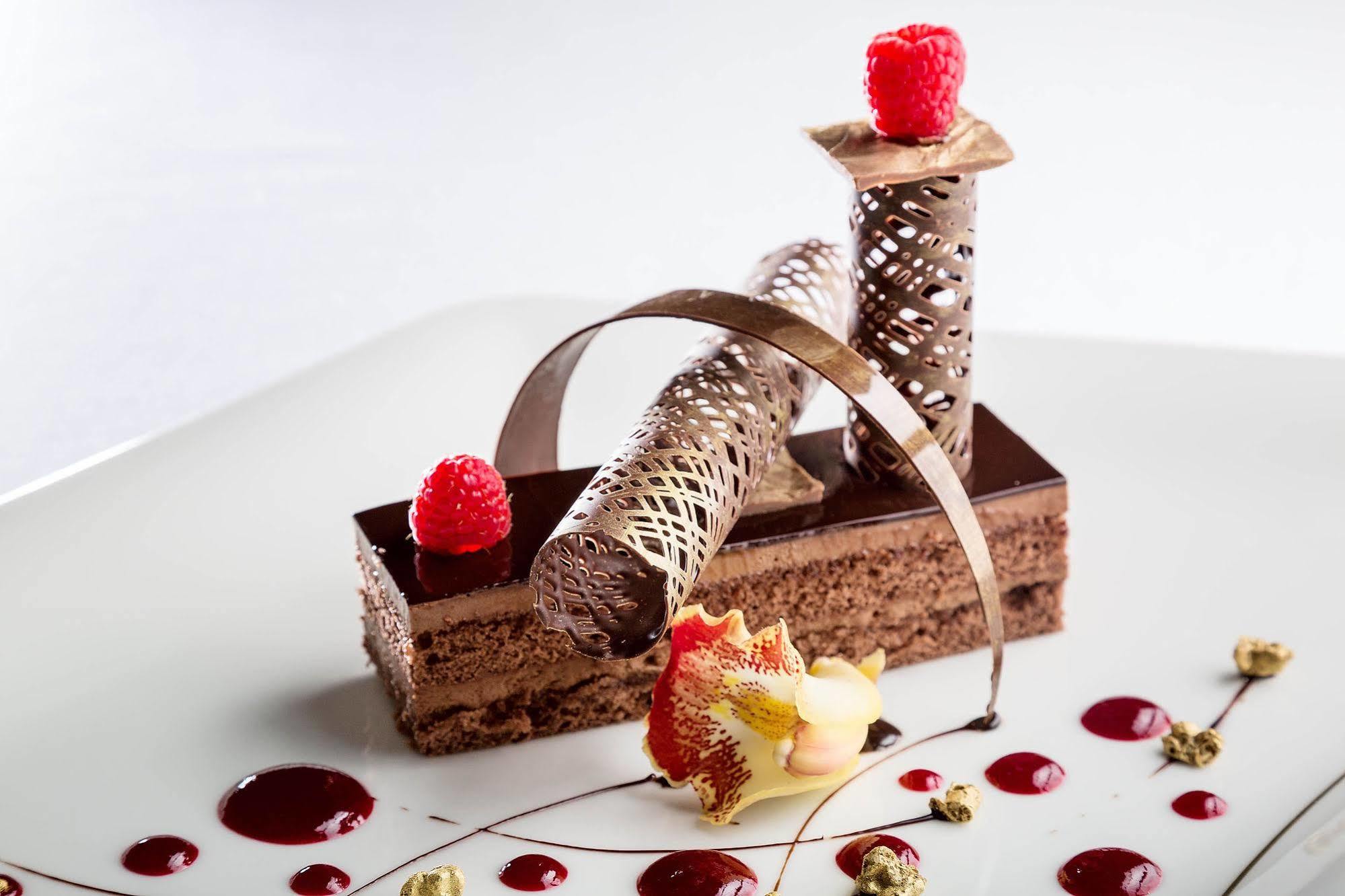 Jabal Omar Hyatt Regency Makkah Hotel Mecca Exterior foto The photo features an artistic dessert presentation. It includes a rectangular chocolate base layered with a rich chocolate mousse or cake. Atop the cake, there are three decorative elements: two cylindrical structures made of intricate chocolate or 