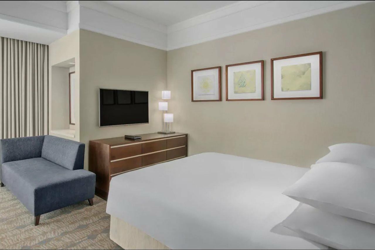 Jabal Omar Hyatt Regency Makkah Hotel Mecca Exterior foto The photo shows a modern hotel room. It features a neatly made bed with white linens and multiple pillows. On the wall opposite the bed, there is a flat-screen television mounted, along with a modern wooden dresser. Above the dresser, three framed ar