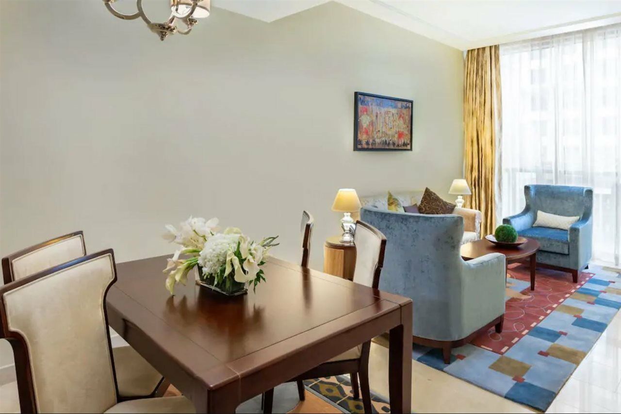 Jabal Omar Hyatt Regency Makkah Hotel Mecca Exterior foto The photo shows an elegantly furnished living space. On the left, there's a wooden dining table with four chairs, decorated with a vase of white flowers. To the right, there are two comfortable blue armchairs and a small side table, each adorned with